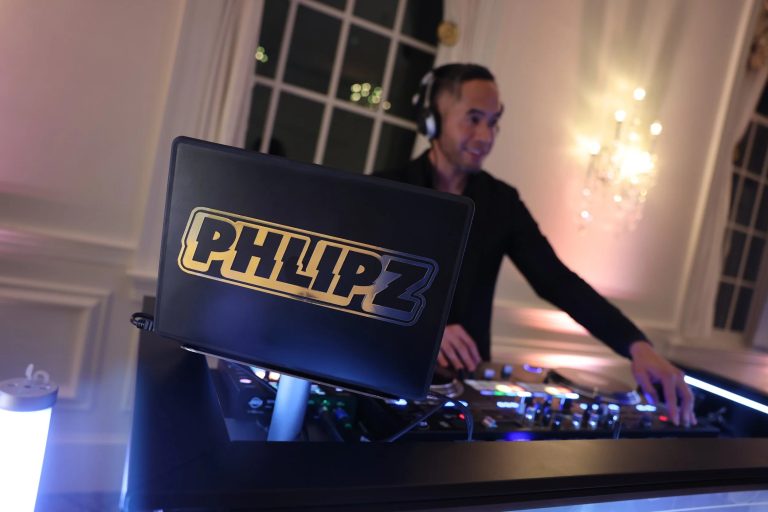 DJ performing at an elegant indoor event with laptop displaying "PHILIP Z" branding and professional mixing equipment
