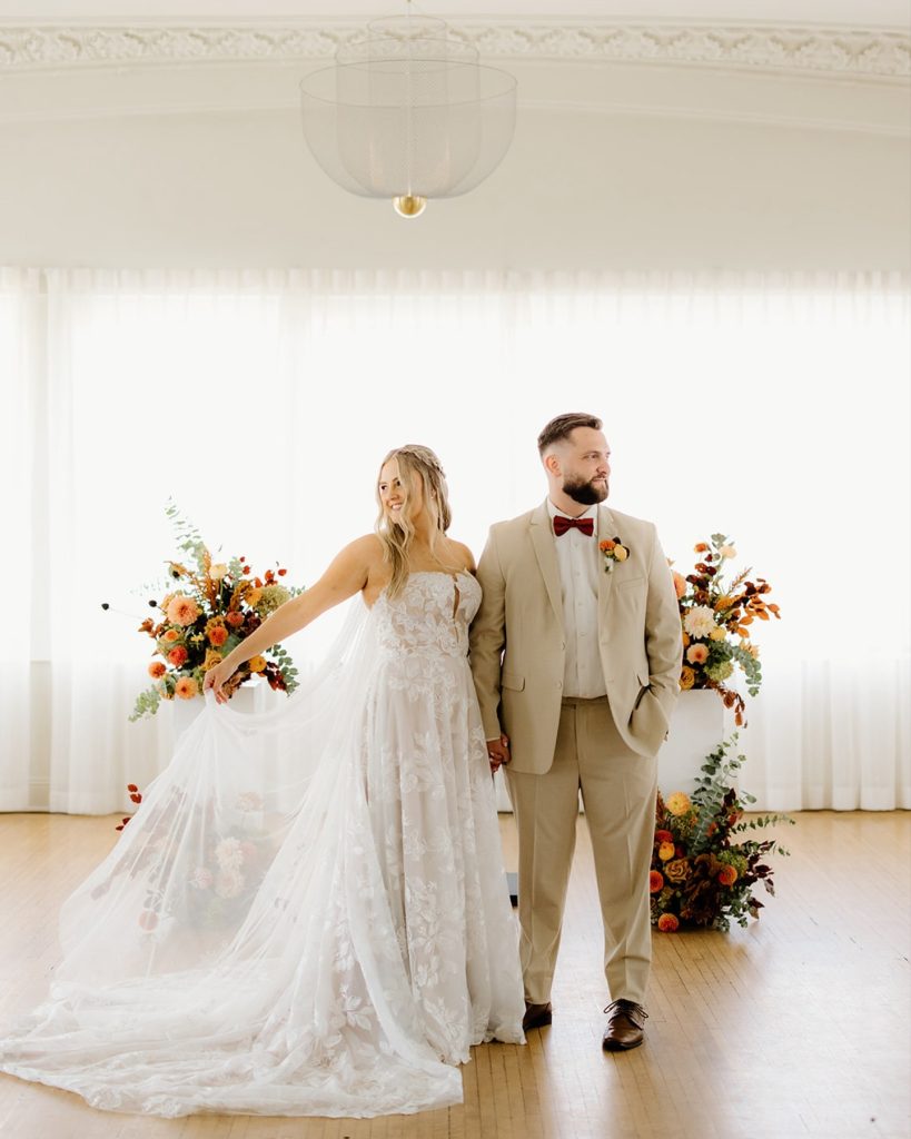 Bride and groom walking hand-in-hand before fall-themed ceremony backdrop with orange floral arrangements