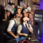 Wedding guests posing in photo booth with props and silly glasses against gold sequin backdrop