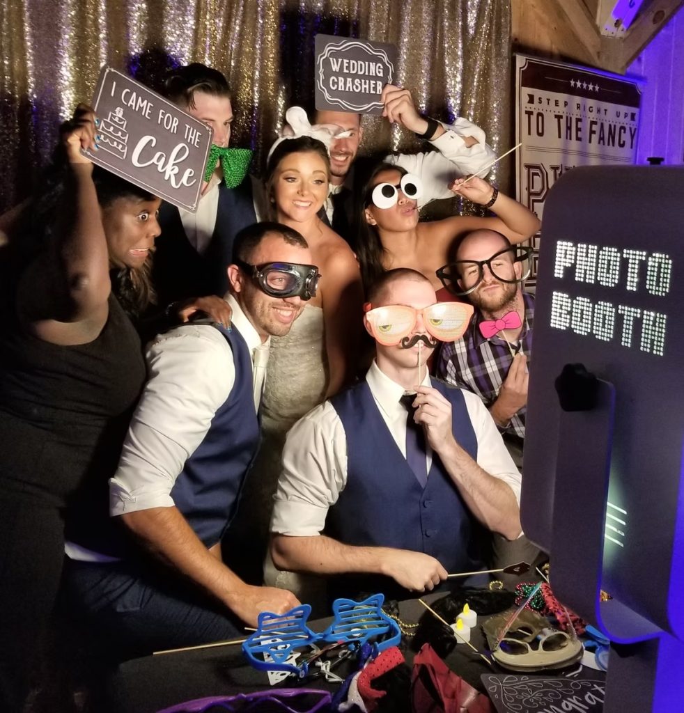 Wedding guests posing in photo booth with props and silly glasses against gold sequin backdrop