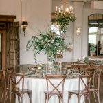 Elegant reception table setting with tall floral centerpiece and wooden cross-back chairs
