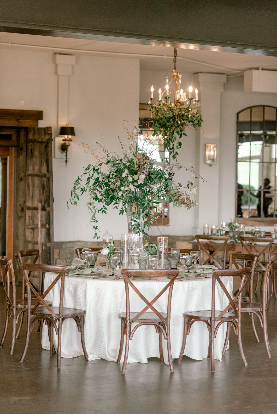 Elegant reception table setting with tall floral centerpiece and wooden cross-back chairs