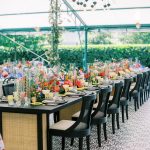 Greenhouse wedding reception with long dining tables, vibrant centerpieces, and mosaic tile flooring