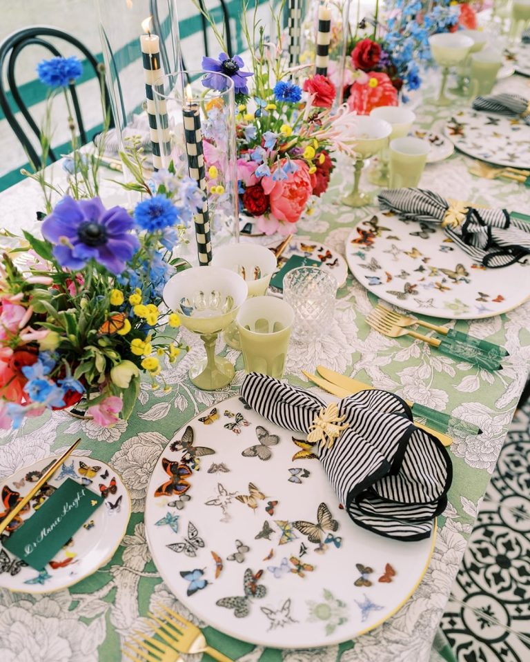 Whimsical place setting featuring butterfly-patterned china, striped napkins, colorful anemones, and yellow glassware