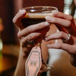 Hands holding beer glass with vintage motel-style keychain wedding favor showing couple's initials