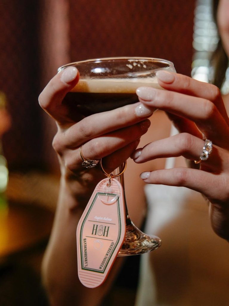 Hands holding beer glass with vintage motel-style keychain wedding favor showing couple's initials