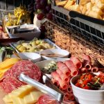 Tiered charcuterie board with assorted cheeses, cured meats, grapes, crackers, and marinated vegetables