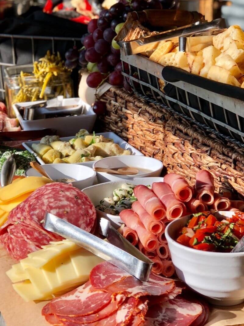 Tiered charcuterie board with assorted cheeses, cured meats, grapes, crackers, and marinated vegetables