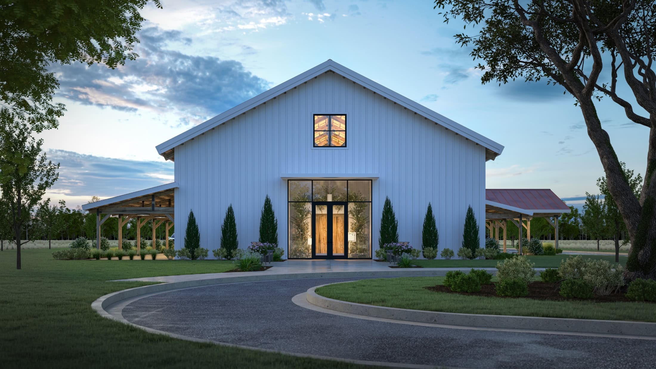 Modern white barn-style wedding venue with illuminated entrance, cypress trees, and circular driveway at dusk