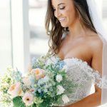 Bride holding lush bouquet of blue, white, and pink flowers with greenery