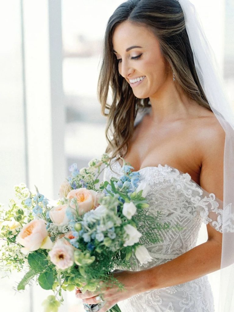 Bride holding lush bouquet of blue, white, and pink flowers with greenery