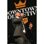 Male vocalist in suit singing passionately on stage with Downtown Collective branded backdrop