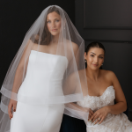Two brides modeling wedding dresses, one in a minimalist strapless gown with veil, the other in a lace embellished dress
