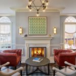 Classic living room with red leather chesterfield sofas, burning fireplace, geometric chandelier, and symmetrical arched windows