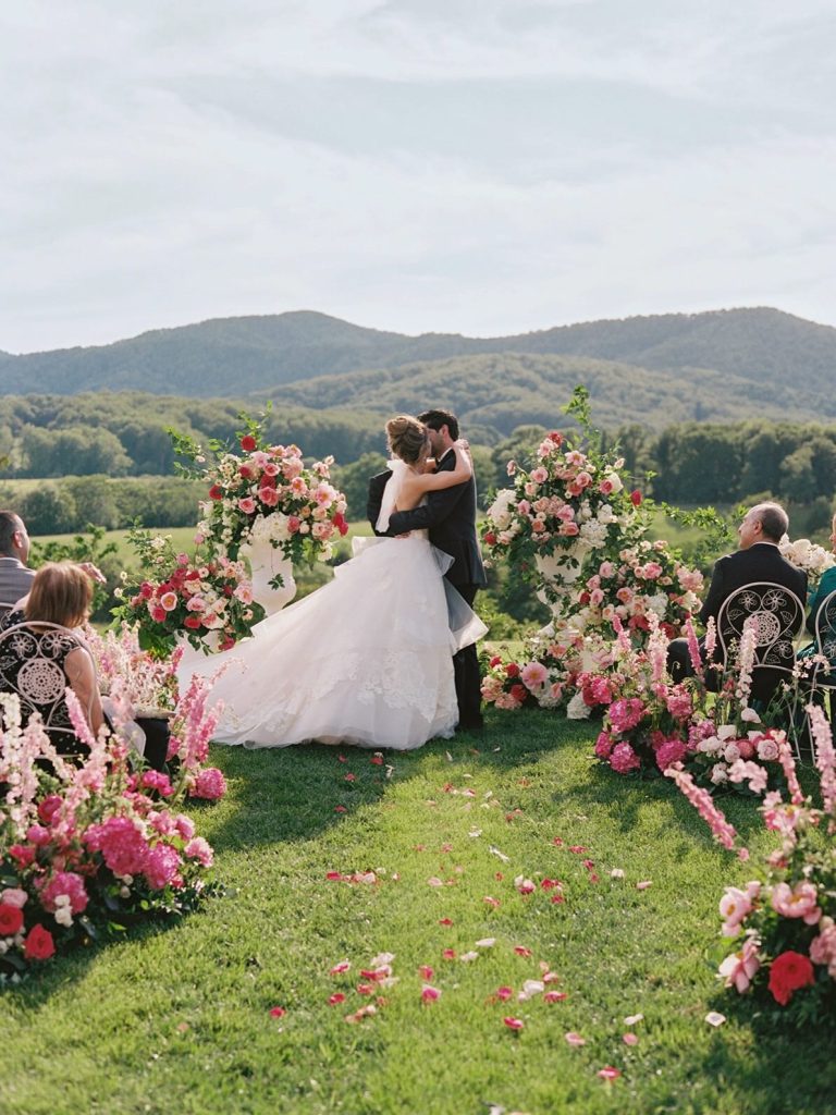 Outdoor mountain wedding ceremony with pink floral arrangements lining the aisle and adorning the ceremony arch