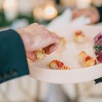 Server holding white plate with golden appetizers at catered event