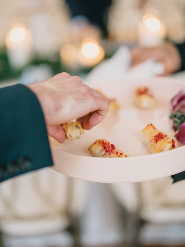 Server holding white plate with golden appetizers at catered event