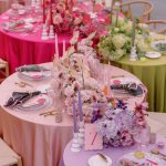 Close-up of ombre-colored reception tables showcasing pink, purple, and green linens with lush floral runners and coordinating place settings