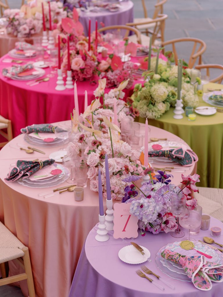 Close-up of ombre-colored reception tables showcasing pink, purple, and green linens with lush floral runners and coordinating place settings