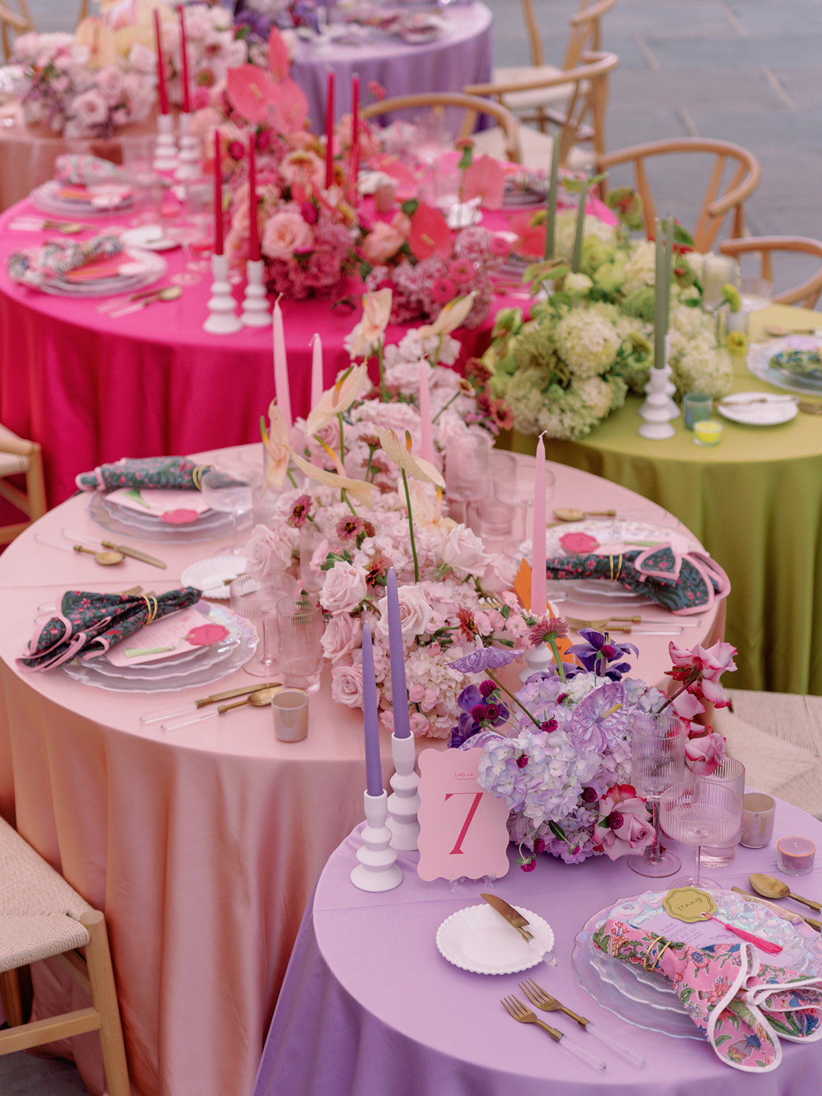 Close-up of ombre-colored reception tables showcasing pink, purple, and green linens with lush floral runners and coordinating place settings