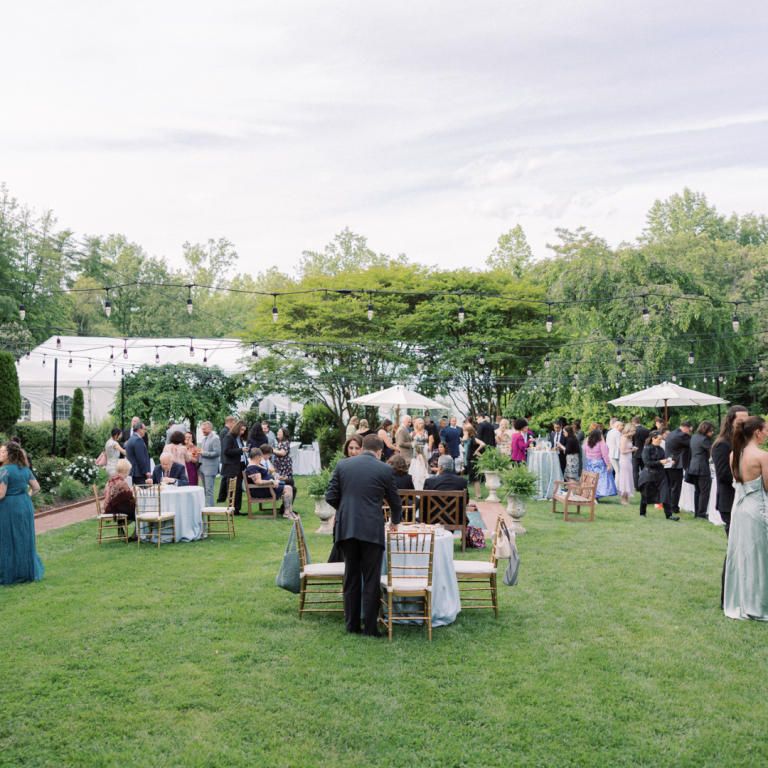 Outdoor wedding reception with white tent and guests mingling on lawn