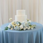 Simple white wedding cake with fresh blue and white flowers on dusty blue tablecloth