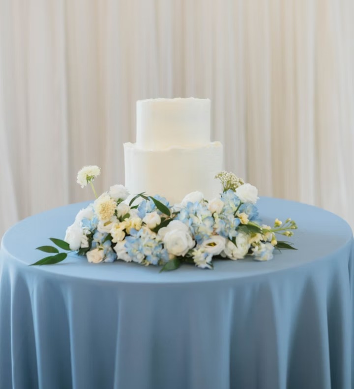 Simple white wedding cake with fresh blue and white flowers on dusty blue tablecloth