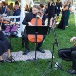 Three-piece string ensemble playing violin and cello for seated wedding ceremony attendees