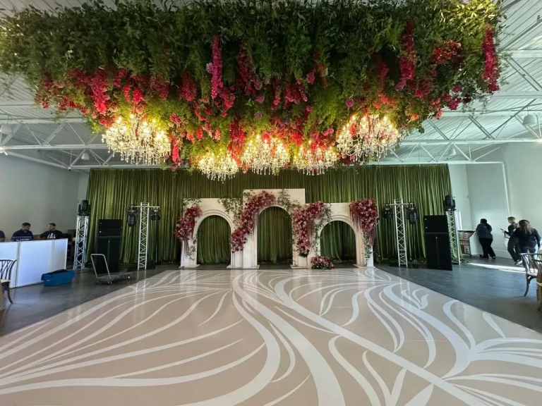 Luxury wedding ballroom featuring hanging floral installation with crystal chandeliers, floral arch backdrop, and custom dance floor