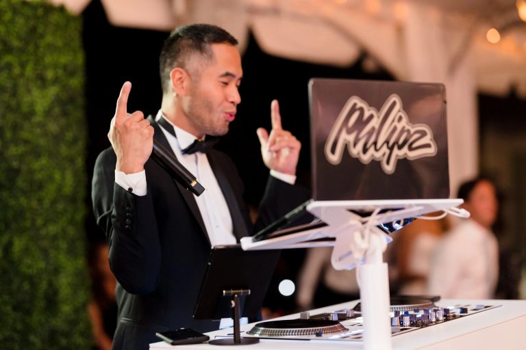 DJ in formal attire gesturing expressively while performing at event with illuminated "Philipz" sign