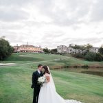 Wedding couple kissing on expansive golf course with overcast sky and resort property in distance