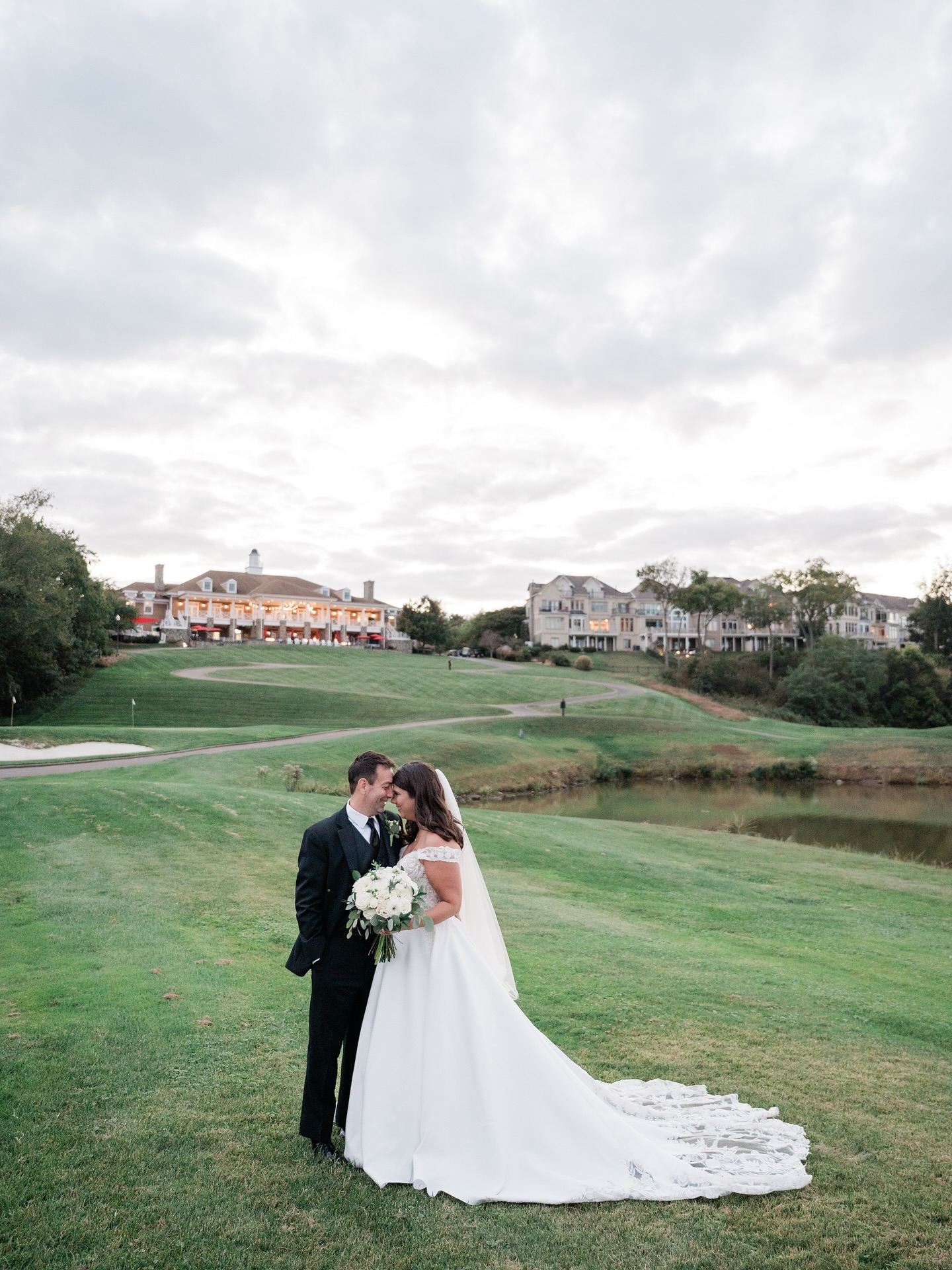 Wedding couple kissing on expansive golf course with overcast sky and resort property in distance