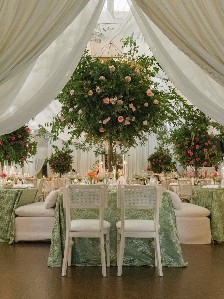 Tented wedding reception with tall tree centerpieces adorned with pink roses