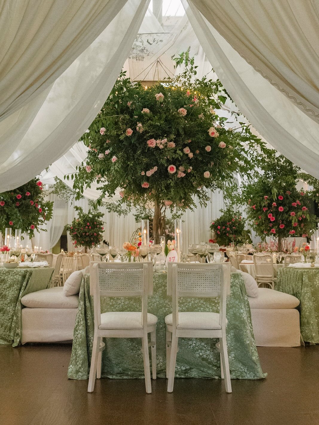 Tented wedding reception with tall tree centerpieces adorned with pink roses