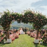 Outdoor wedding ceremony with floral arch and guests seated on lawn