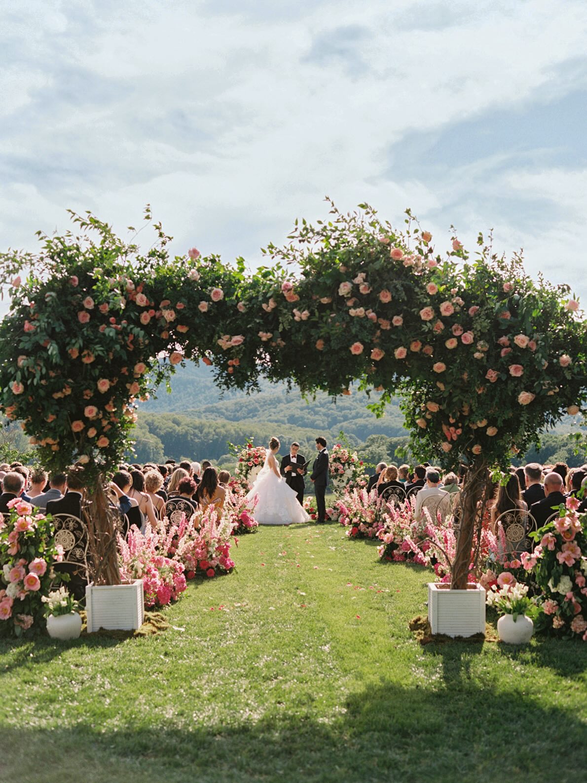 Outdoor wedding ceremony with floral arch and guests seated on lawn