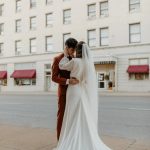 Bride and groom in intimate embrace on urban street, bride's cathedral train flowing behind them