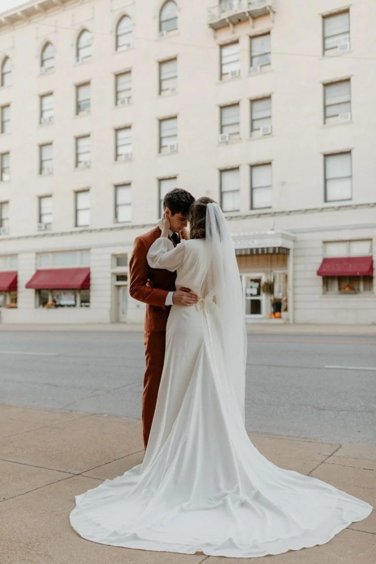 Bride and groom in intimate embrace on urban street, bride's cathedral train flowing behind them