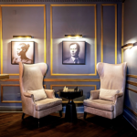 Two cream wingback chairs flanking small round table beneath portrait gallery wall with navy and gold paneling