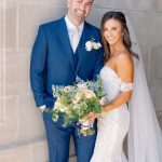 Newlyweds smiling together, groom in navy suit and bride in lace gown with pastel bridal bouquet