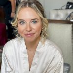 Blonde bride in white satin robe with soft curled updo during wedding preparation