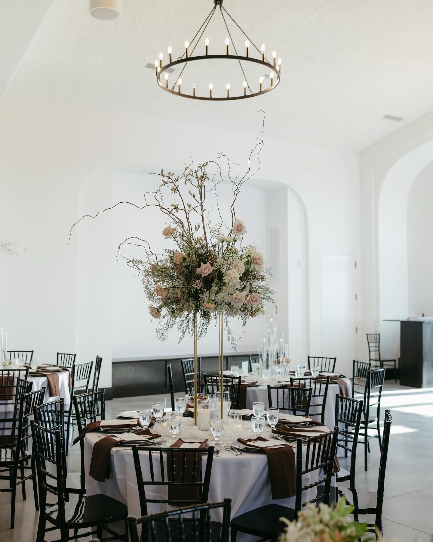 Round reception table with dramatic tall centerpiece of roses, greenery, and curly willow branches