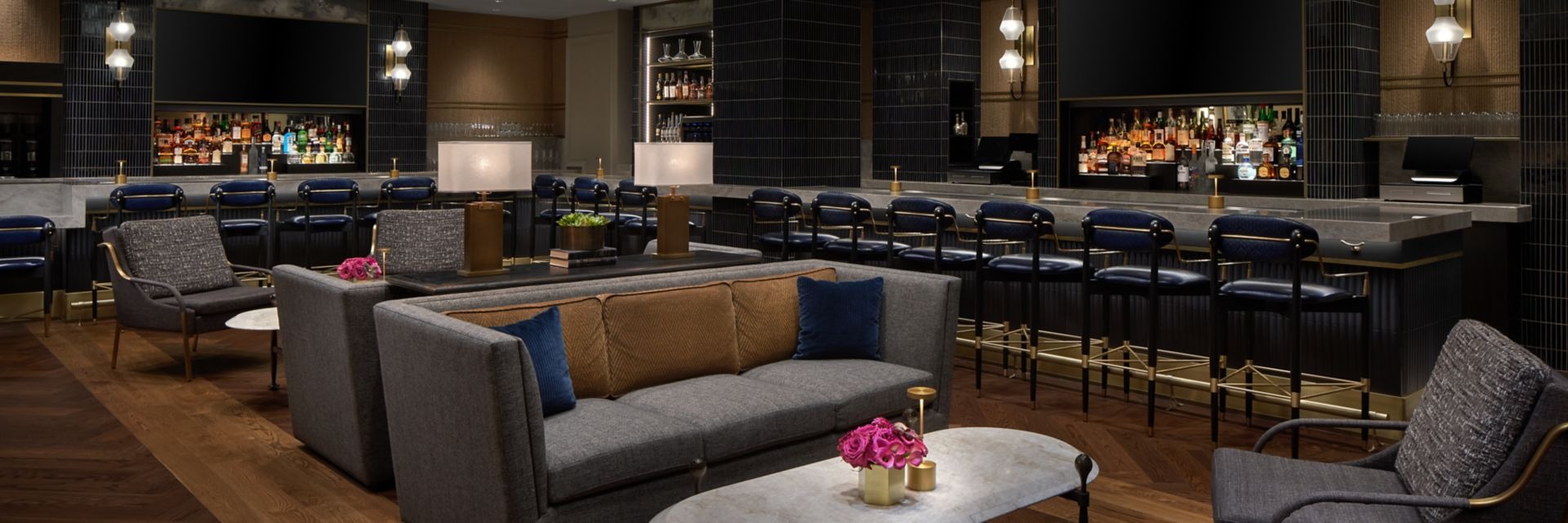 Modern lounge area with tan leather sofa, navy accents, and pink floral centerpiece on marble table
