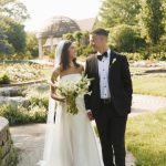 Bride and groom holding hands in formal attire at outdoor garden wedding venue