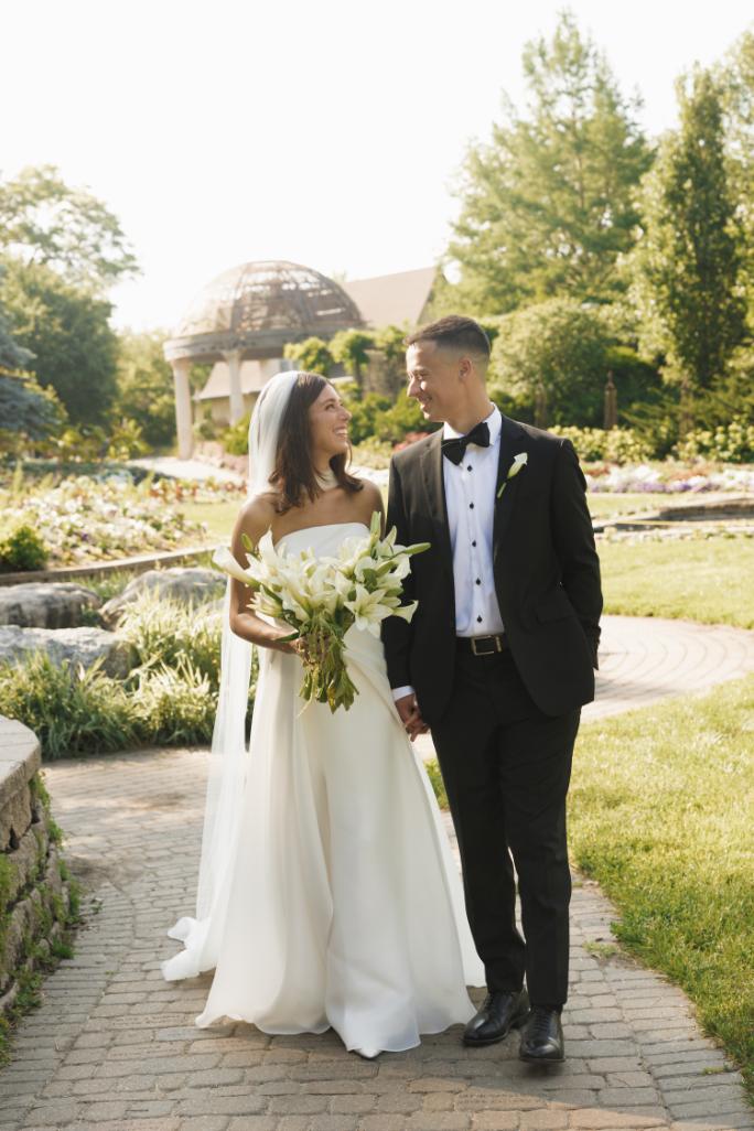 Bride and groom holding hands in formal attire at outdoor garden wedding venue