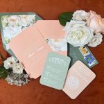 Elegant wedding paper goods in soft peach and green tones styled with white garden roses