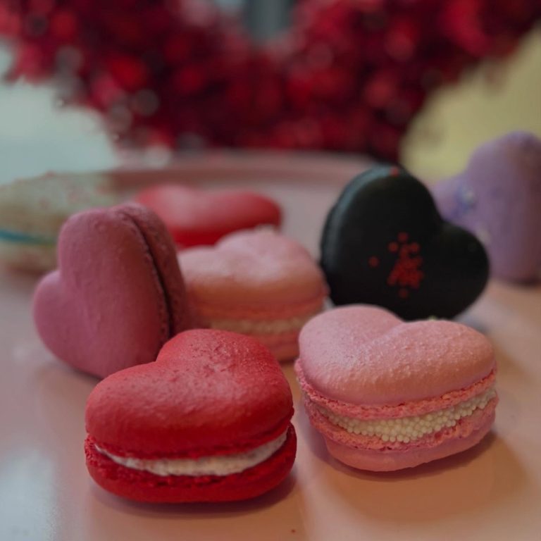 Assortment of heart-shaped and round macarons in pink, red, and black with decorative details