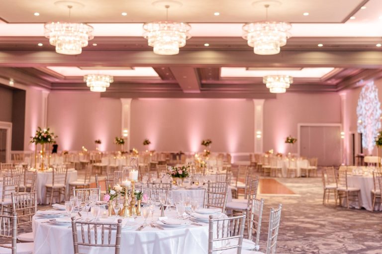 Elegant ballroom reception space with coffered ceiling, statement chandeliers, round tables, and rose gold accent lighting