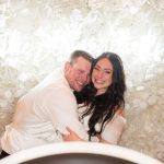 Couple laughing together in photo booth with cream and white floral backdrop