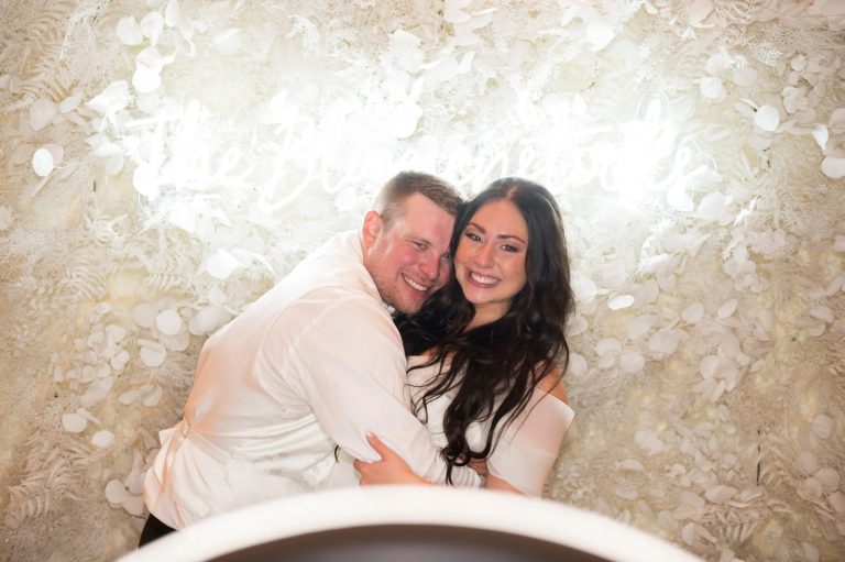 Couple laughing together in photo booth with cream and white floral backdrop